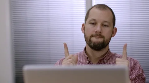A bearded office worker thinking at work in front of silver laptop.  Video stock 73124044