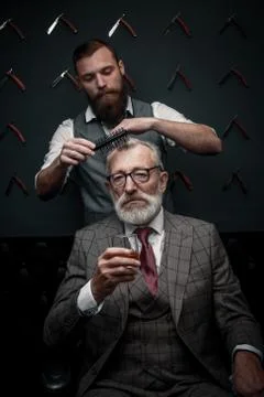 Bearded old businessman sitting at barber shop in chair choosing haircut design Stock Photos