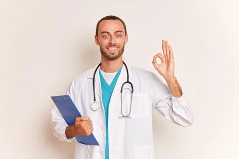 Bearded practitioner stands on blue background wearing white coat with Stock-Fotos