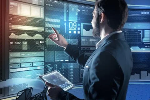 Bearded programmer pointing to his computer while holding a transparent device Stock Photos