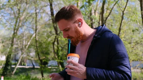 Bearded red-haired man drinks coffee from straw from disposable cup and use his Stock Footage 170267980