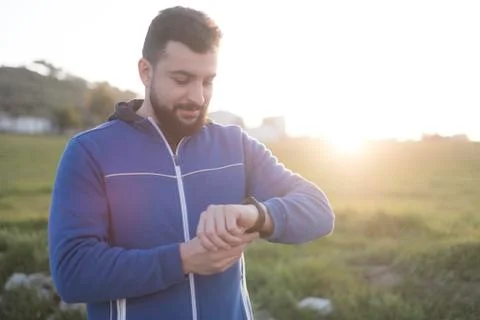 Bearded runner resting after training outdoors looking smart watch Foto stock