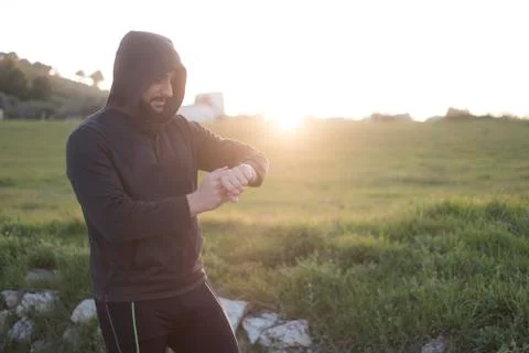 Bearded runner resting after training outdoors, looking watch Stock Photos