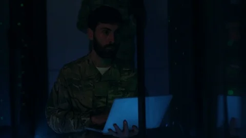 Bearded soldier working on laptop intercepting network data from server room Stock Footage 121270908