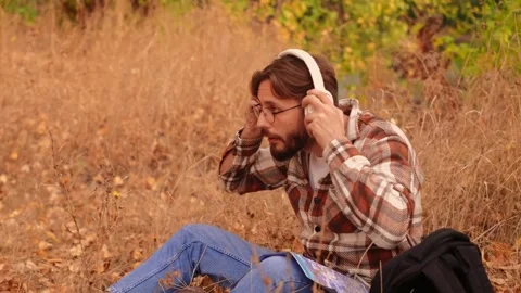 Bearded white man with glasses puts on white headphones, enjoying nature, high-q Stock Footage 278277401