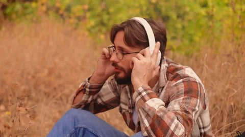Bearded white man with glasses puts on white headphones, enjoying nature, high-q Stock Footage 278277403