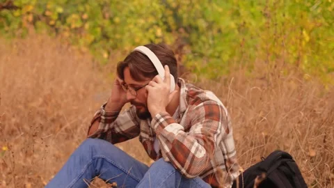 Bearded white man with glasses puts on white headphones, enjoying nature, high-q Stock Footage 278277611