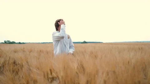 A bearded young farmer stands in a wheat field and folds his arms admiring the Stock Footage 134579820