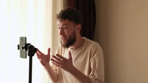 A bearded young guy communicates via video using a phone mounted on a tripod. Stock Footage 278798355