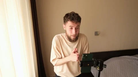 A bearded young guy communicates via video using a phone mounted on a tripod. Stock Footage 278798479
