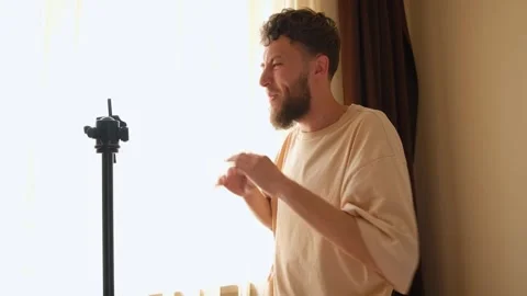 A bearded young guy communicates via video using a phone mounted on a tripod. Stock Footage 278798512