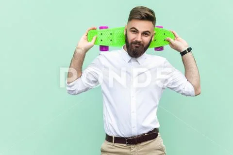 Bearded young hipster looking at camera, holding penny skateboard under his h Stock Photos