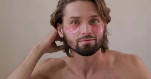Bearded young man with bare torso applying korean patches under eyes while Stock Footage 142527269