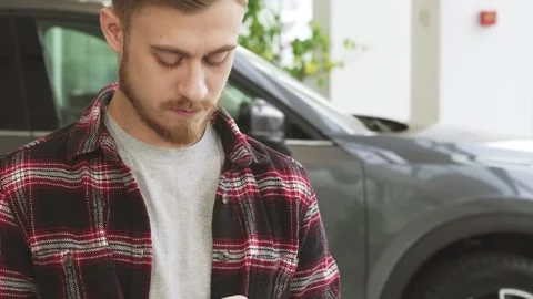 Bearded young man confidently using smartphone while purchasing a new car at the Stock-Footage 311984575