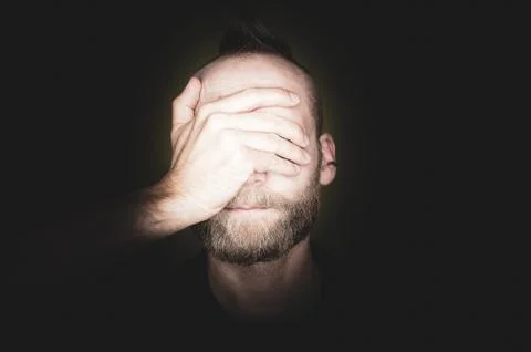 A bearded young man covers his eyes with one hand. Stock Photos