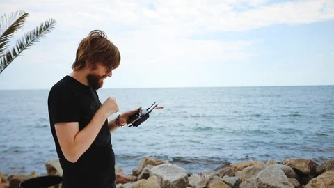 Bearded young man pilots drone at ocean coast on windy day Stock Footage 113788061