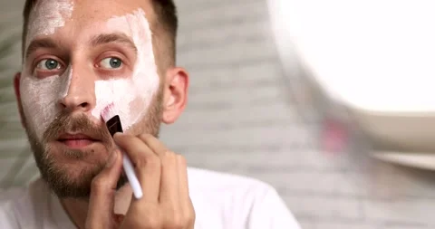 Bearded young man in white t-shirt using brush for applying cosmetic mask on Stock Footage 142536719