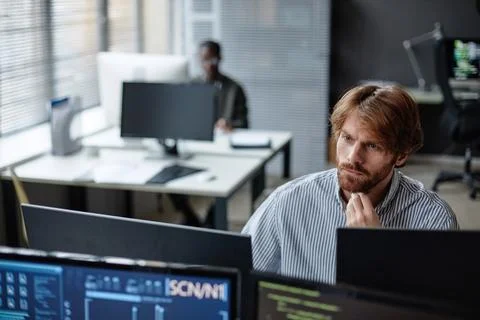 Bearded Young Man Working with Multiple Computers Foto stock
