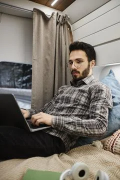 Bearded young man working in trailer van using computer on bed Foto stock