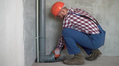 Bearded young plumber fitting pvc sewage pipes inside newly built house Stock Footage 219542933