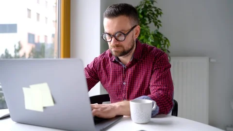 Beared man in glasses sitting at home office and working on a laptop Stock Footage 102217546