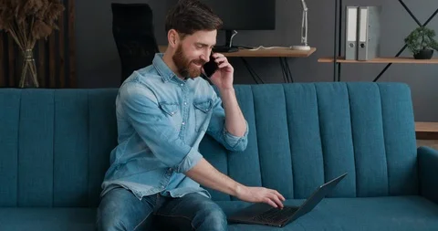 Beared Satisfied freelancer using laptop Device leaning on Sofa at Home office Stock Footage 127462104