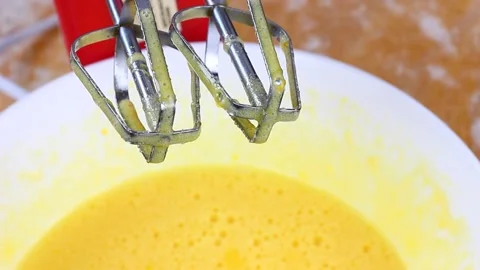The beaten eggs drip from the blender into a white deep bowl with a yellow egg Stock Footage 146432246