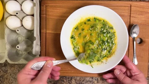 Beating raw chicken eggs and parsley in a plate with a fork to make an omelette. Stock Footage 300454095