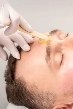 Beautician applying wax paste between eyebrows during the procedure of waxing in Stock Photos