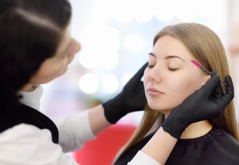 Beautician combs eyebrows using special brush on face young beautiful model.  Stock Photos