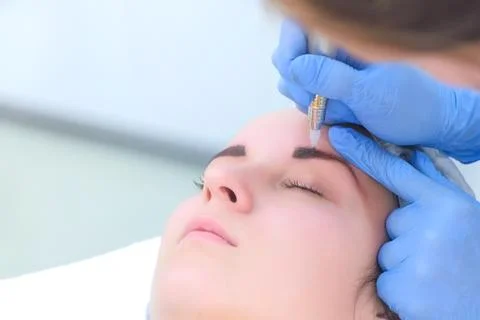 Beautician making eyebrows microblading procedure in beauty salon for woman. Stock Photos