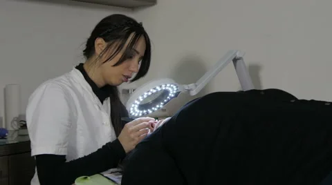 Beautician using magnifying glass and cosmetic equipment for eyelash extensions. Video stock 59574393