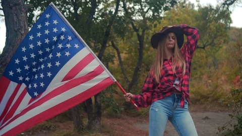 Beautiful and sexy girl in a cowboy hat and a red shirt stands with an American Stock Footage