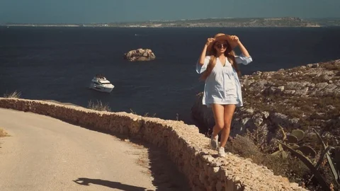 Beautiful asian girl is walking on a stone barrier in a hat and sunglasses Stock Footage