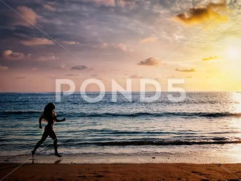 Beautiful athletic woman running along sea beach in the morning Stock Photos