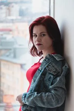 Beautiful attractive girl with red hair in a blue denim jacket and red dress  Stock Photos