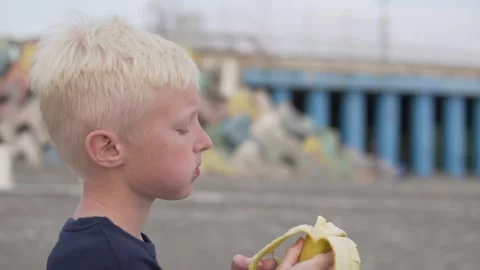 Beautiful baby boy blond eats a banana in the street during a walk. Stock Footage 142575095