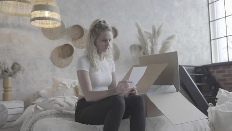 Beautiful Blond Girl Reading Instructions Sheet While Sitting On Bed Stock Footage