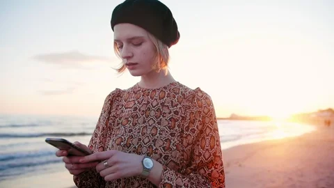 Beautiful blond girl texting using phone on the beach in sunset light. Young Stock Footage 105745581