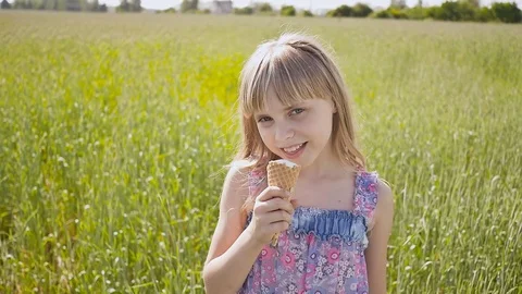 Beautiful blond little girl eats ice-cream in the summer next to the wheat field Stock Footage