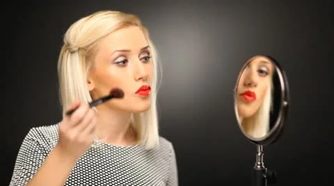 Beautiful blond model applying foundation make-up with a brush in the mirror Stock Footage 10583863