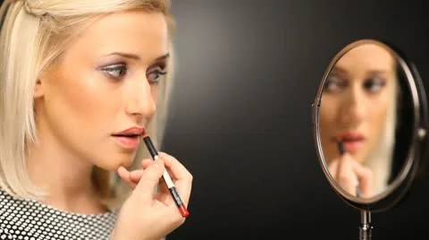 Beautiful blond model applying liner to contour her lips in the mirror Stock Footage