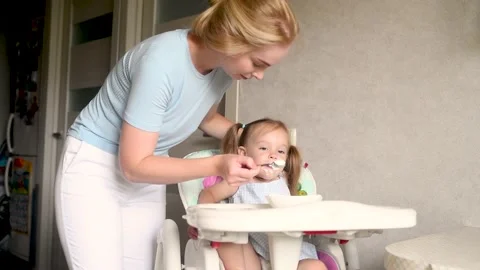 Beautiful blond mother feeds a funny little daughter of 2 years old with a spoon Stock Footage