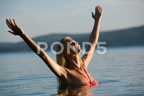 Beautiful blonde bathing in blue water with her arms raised and eyes closed Stock Photos