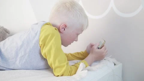 A beautiful blonde boy flips through a news feed on his mobile phone at home on Stock Footage 133245847