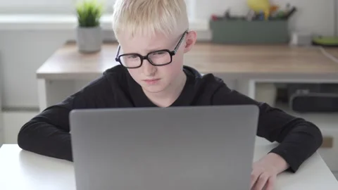 A beautiful blonde boy with glasses learn remotely from home at the computer Stock Footage 154936155