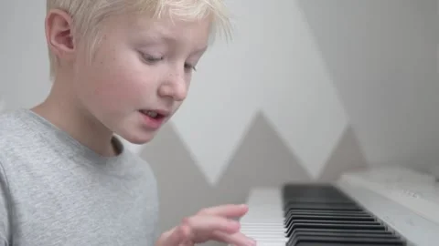 A beautiful blonde boy learns to play the electronic piano at home Stock Footage 145456915