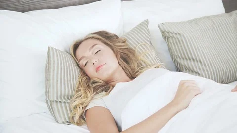 Beautiful blonde in her bed opens her eyes, wakes up and stretches Stock Footage 76142115
