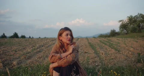 Beautiful blonde model in brown jacket sitting on plowed field Stock Footage 221461410