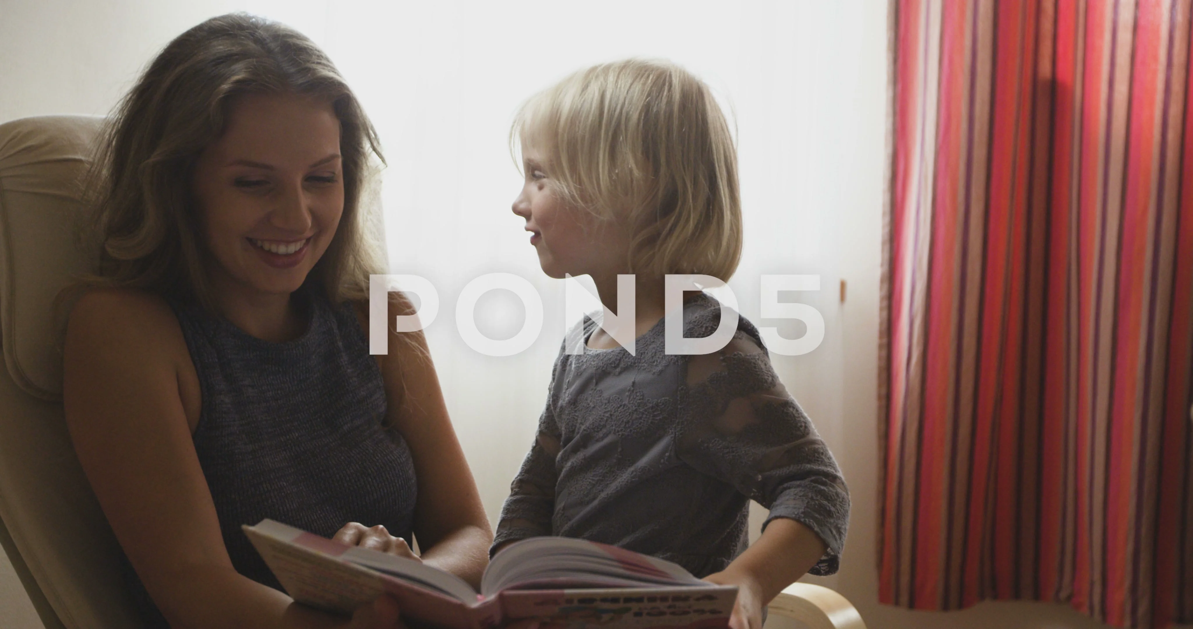 Beautiful blonde mom reading a book to a daughter sitting in chair